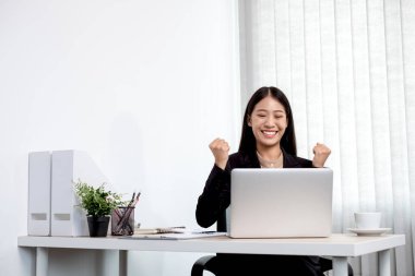 Ofiste çalışırken mutlu ve neşeli bir gülümsemeyle dizüstü bilgisayarda çalışan Asyalı iş kadını..