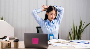 Asyalı kadın muhasebeci, ofiste çalışırken rahatlamak ve dinlenmek için sandalyede çalışmaktan yoruldu..