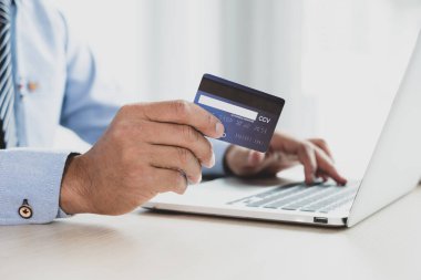İş adamının elinde bir kredi kartı var ve ofisteki online alışveriş ve internet ödemeleri için dizüstü bilgisayar kullanıyor..