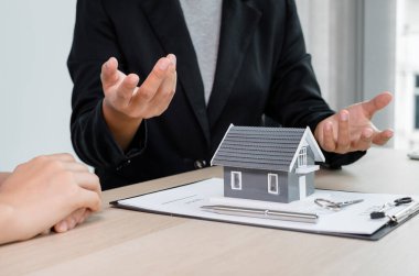 Ev modeli olan bir emlakçı ev kiralamak ve ev sigortası almak için müşterilerle konuşuyor. Ev kiralama ve sigorta konsepti.