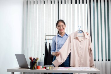 Tekstil aksesuarları ve girişimci tasarımcı çizimleriyle genç ve güzel Asyalı moda terzisi stüdyoda yaratıcı fikirler için dizüstü bilgisayarı olan parlak renklerle dolu..