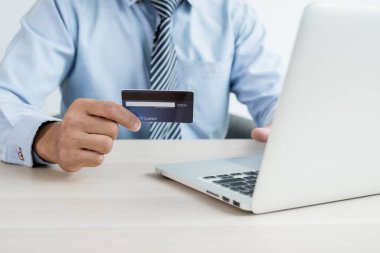 İş adamının elinde bir kredi kartı var ve ofisteki online alışveriş ve internet ödemeleri için dizüstü bilgisayar kullanıyor..