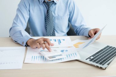 İş adamının eli masalarında oturur ve yatırımlarıyla ilgili sonuçları gösteren finansal grafikleri hesaplar, başarılı bir iş büyüme süreci planlar.