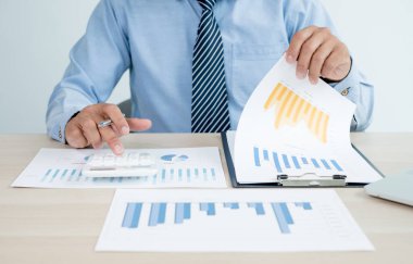 İş adamının eli masalarında oturur ve yatırımlarıyla ilgili sonuçları gösteren finansal grafikleri hesaplar, başarılı bir iş büyüme süreci planlar.