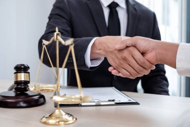 Hukuk bürosunda çalışan profesyonel erkek avukatların tokalaşması için teraziler, adalet terazileri, yargıç tokmağı ve dava belgeleri var. Hukuk ve adalet kavramları.