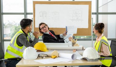 Erkek ve kadın mühendisler ve mimarlardan oluşan bir ekip, çalışma ekibi, inşaat planlarını tartışıyor ve çiziyor, baskı yapıyor, inşaat alanlarında yazıyor..