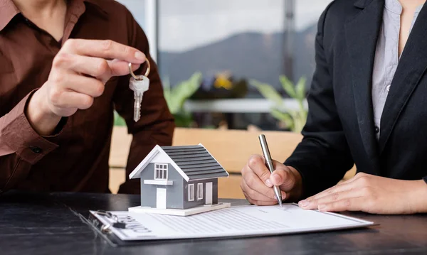 A real estate agent broker hand over the house key to the new owner after completing the signing according to the agreement renting a house and buy the house insurance.