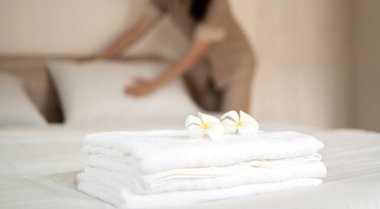 Bir otel hizmetçisi yataktaki havluları istifledi ve otel odasındaki havluların üzerine çiçekler koydu..