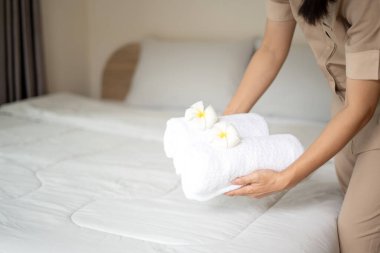 Bir otel hizmetçisi yataktaki havluları istifledi ve otel odasındaki havluların üzerine çiçekler koydu..