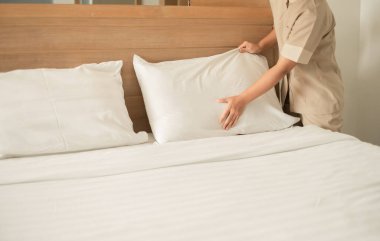 Otel hizmetçisi otel odasını temizler ve yatağı toplar..
