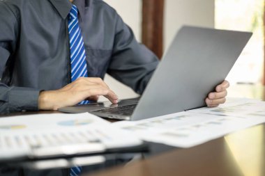 Asyalı işadamı masalarında oturuyor ve yatırımlarıyla ilgili sonuçları gösteren mali grafikleri hesaplıyor, başarılı bir iş büyüme süreci planlıyor.