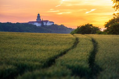 Pannonhalma Archabbey with wheat field and path on sunset clipart