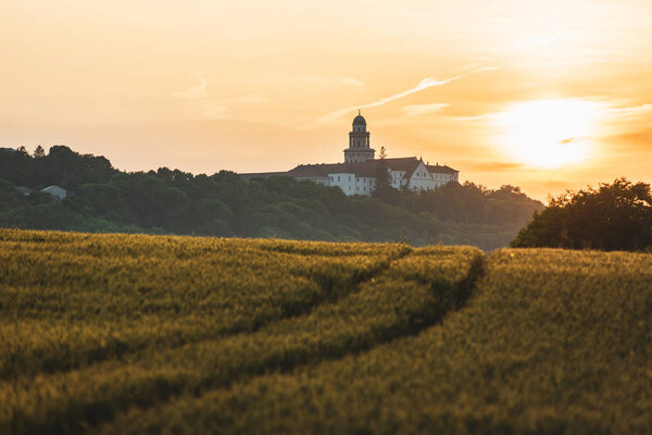 Pannonhalma Archabbey with wheat field and path on sunset time in summer