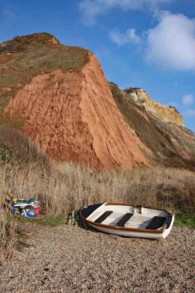 En roddbåt och fiskeredskap vid basen av Sandstensklipporna i Juraeran stiger från Salcombe Regis Beach — Stockfoto