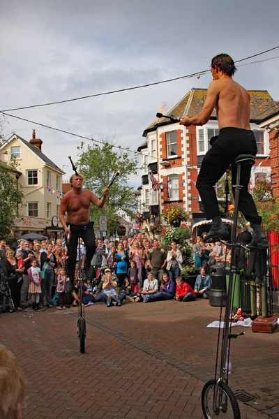 Sidmouth, Devon, England-5 augusti 2012: två Street jonglörer och underhållare uppträda med enhjulingar och eld klubbar på torget till en uppskattande publik under folk veckan — Stockfoto