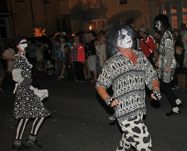 Sidmouth, Devon, England-10 augusti 2012: en dans trupp klädd i mycket kusliga svarta och vita kostymer delta i natten stängning procession av folk veckan. — Stockfoto