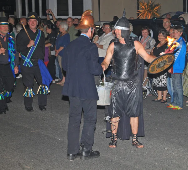 Sidmouth, Devon, England-10 augusti 2012: en man klädd som en brandman och en annan klädd som en forntida krigare delta i natten stängning procession av folk veckan — Stockfoto