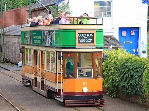 Colyton, devon, england - 6. August 2012: eine orangefarbene und grüne straßenbahn fährt in die station colyford auf der seaton straßenbahn ein. Passagiere reisen für ein besonderes Ereignis an. — Stockfoto