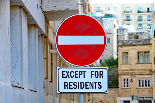 Red and white circular no entry sign except for residents in front of a block of apartments.