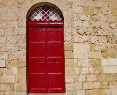 Sliema, Malta 'da kireç taşından bir duvarda yeni boyanmış kırmızı bir kapı.