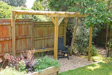 OTTERY St. Mary, DEVON, İngiltere - 25 Temmuz 2019: Bir İngiliz kır bahçesinde bir pergola ve bir manolya ağacının gölgesinde bir şezlong yerleştirilmiştir.