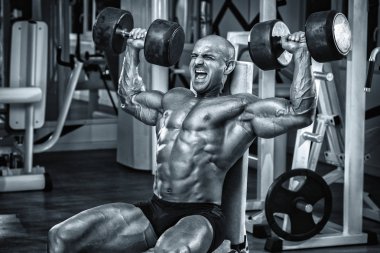 Vücut geliştirici spor salonunda dambıllarla egzersiz yapıyor.