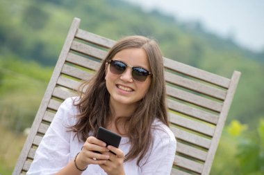 güzel genç kız bununla birlikte güneş gözlüklü bir akıllı telefon kullanıyor