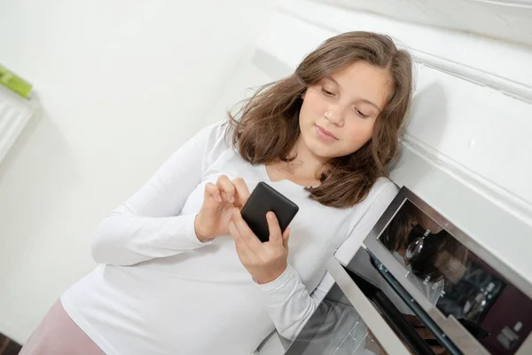 一个在厨房里用智能手机的少女 — 图库照片