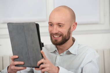 Gülümseyen sakallı genç adam dijital tablet kullanıyor.