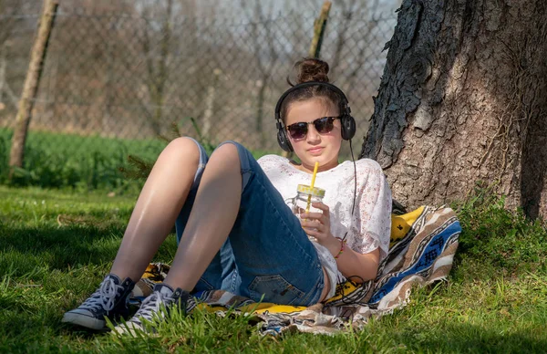 Девочка-подросток слушает музыку и пьет воду в парке — стоковое фото