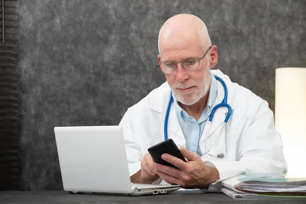 Senior bebaarde arts lezen bericht op telefoon — Stockfoto