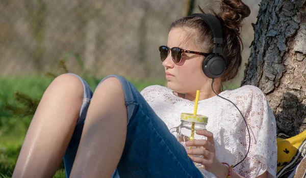 Teenager girl listening music and drinking water in the park — Stock Photo, Image