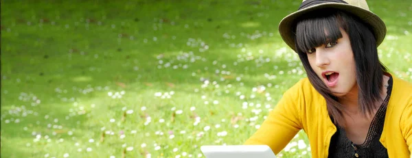Mladá brunetka se žlutým svetrem pomocí tabletu v parku — Stock fotografie