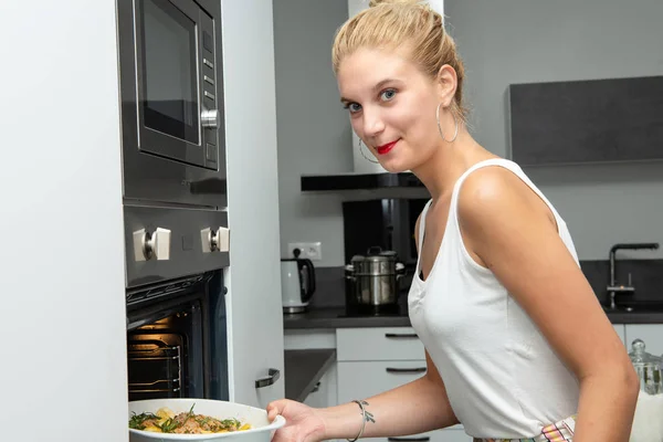 Glimlachende jonge blonde vrouw bereidt de maaltijd in de keuken — Stockfoto
