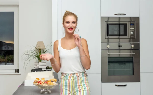 Mooie jonge blonde vrouw die taarten eet in de keuken — Stockfoto