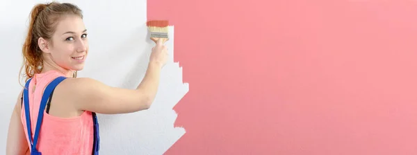 Pretty young woman painting the wall pink color, horizontal phot — Stock Photo, Image
