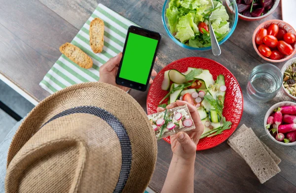 Kvinna äter en vegan sallad och med hjälp av en smartphone, grön skärm, — Stockfoto
