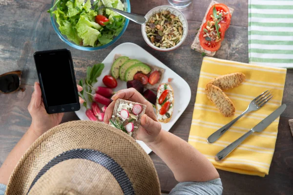 Femme manger une salade végétalienne et en utilisant un smartphone, vue de dessus — Photo