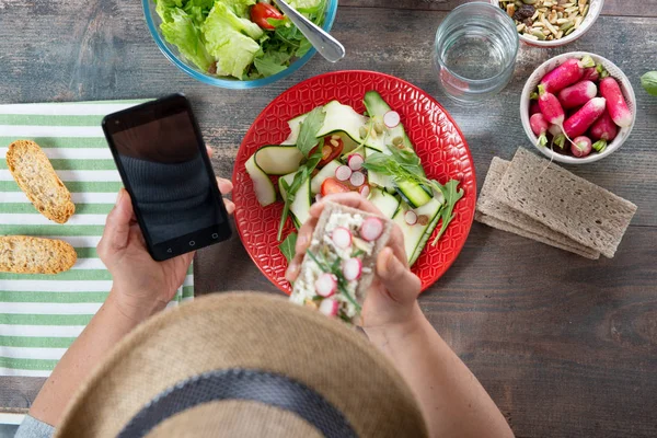 Kvinna äter en vegan sallad och använder smartphone, ovanifrån — Stockfoto