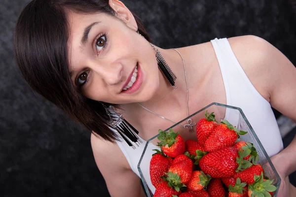 सुंदर युवा ब्रुनेट महिला स्ट्रॉबेरी के एक कटोरे के साथ — स्टॉक फ़ोटो, इमेज
