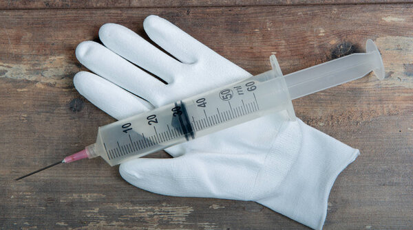 white gloves with big syringe on wooden background