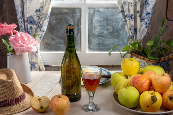 Bottle and glass of cider with apples. near the window, in the r — Stock Photo, Image