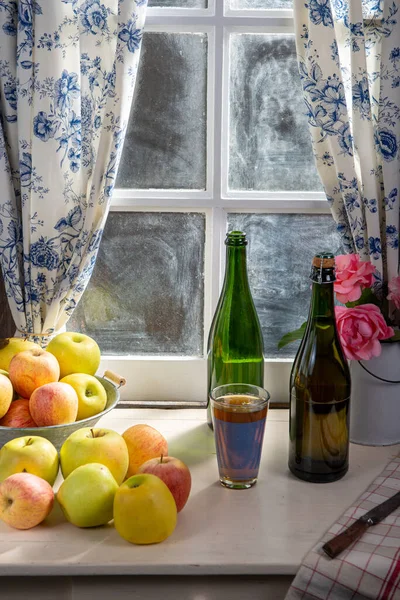 Bottle and glass of cider with apples. near the window, in the r — Stock Photo, Image