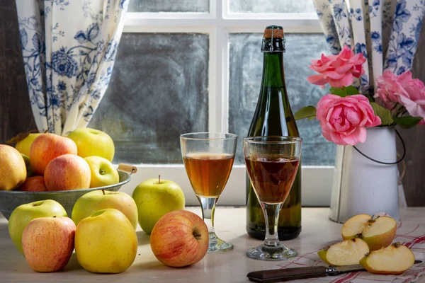 Bottle and glasses of cider with apples, near the window, in rus — Stock Photo, Image