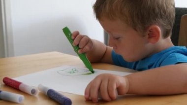 Küçük şirin çocuk bir kağıt parçasına renkli kalemler çiziyor.