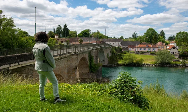 a woman looking Ancient bridge over the river Gave d`Oloron at town of Navarrenx, France.