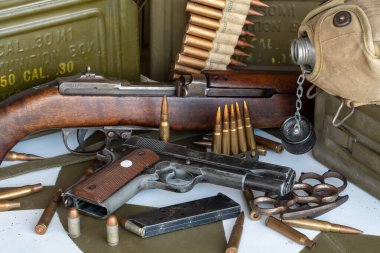 Masanın üzerinde silah ve bir kutu mermi var. Silah bir Colt 45. Silahın etrafına saçılmış bir sürü mermi var.