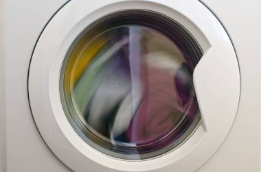 Çamaşır makinesi kapısı ve içinde dönen giysiler.