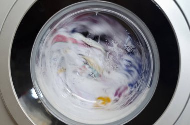 Çamaşır makinesi kapısı ve içinde dönen giysiler.