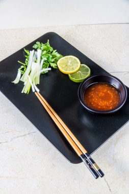 Boşaltmak için oryantal yiyecek, chop sopa, kireç, limon, taze soğan, scallions ve tatlı biber sos daldırma plakalı siyah altıgen.